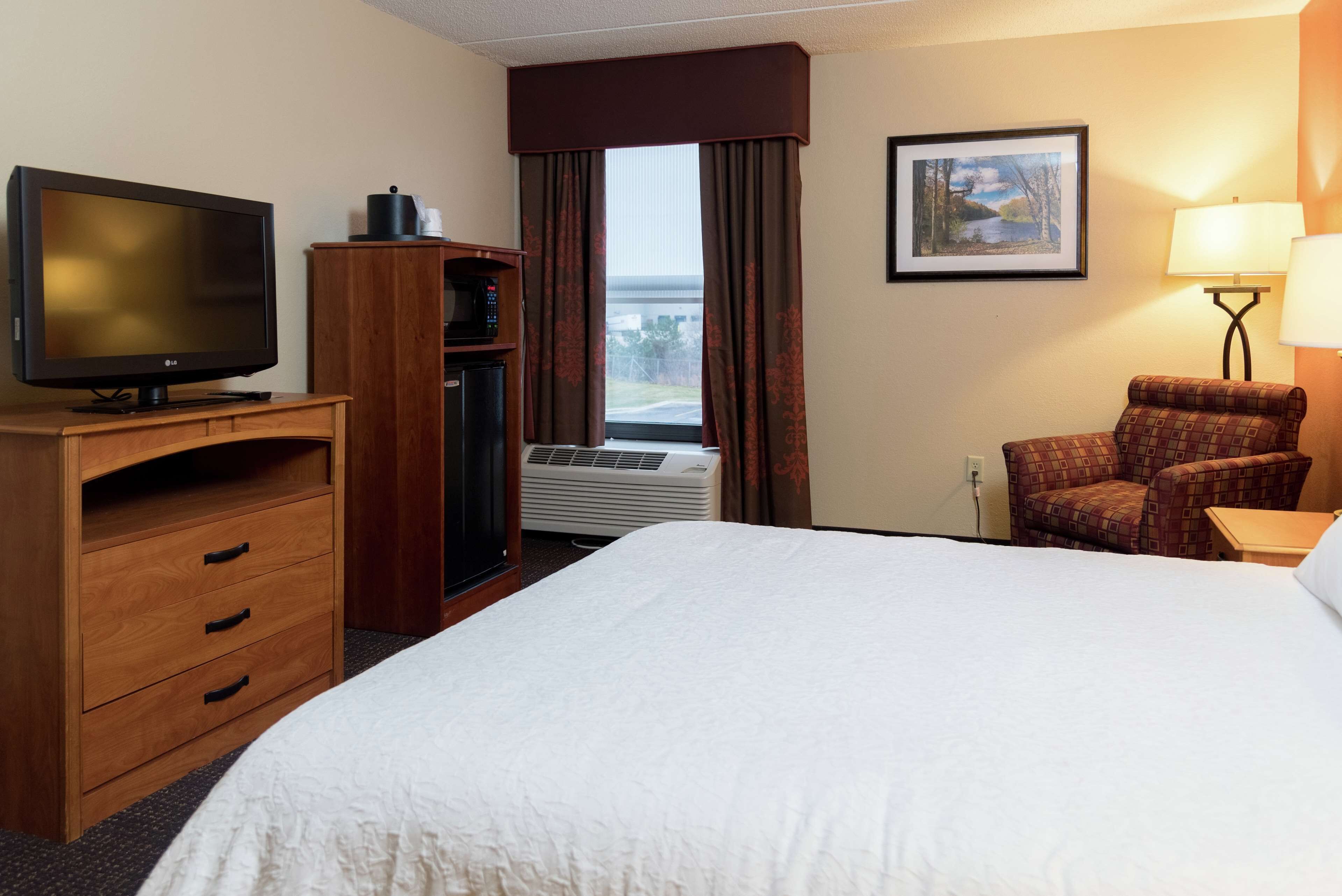 A hotel room with a large bed, a television, a desk with a computer, a chair, and a window with curtains.