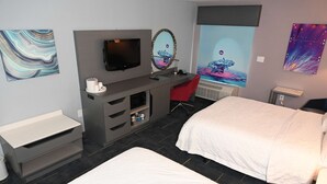 Habitación de hotel moderna con cama, escritorio con televisor de pantalla plana, una silla roja y obras de arte en las paredes.