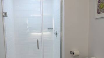 A bathroom with a glass-enclosed shower, a toilet, and a white tiled wall.