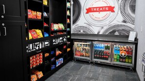 Zona de venta automática con múltiples estantes llenos de aperitivos y una sección refrigerada con diversas bebidas.