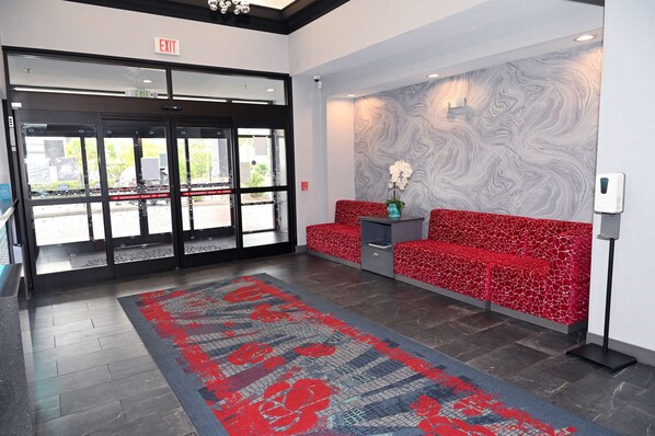 A hotel lobby with a red patterned sofa, a marble wall, and a red and blue patterned carpet.