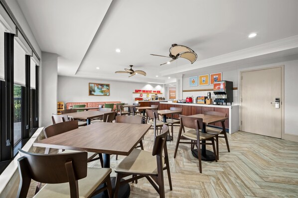 Un restaurante moderno con mesas y sillas de madera, ventiladores de techo y una zona de cocina con una máquina de café.