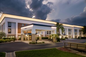 A modern hotel with a covered entrance, a parking lot, and well-maintained landscaping.