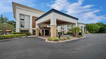 A modern hotel with a covered entrance, a parking lot, and landscaped areas.