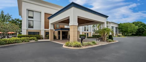 A modern hotel with a covered entrance, a parking lot, and landscaped areas.