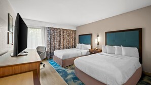 Habitación de hotel con dos camas, un escritorio, un televisor y una cortina estampada.