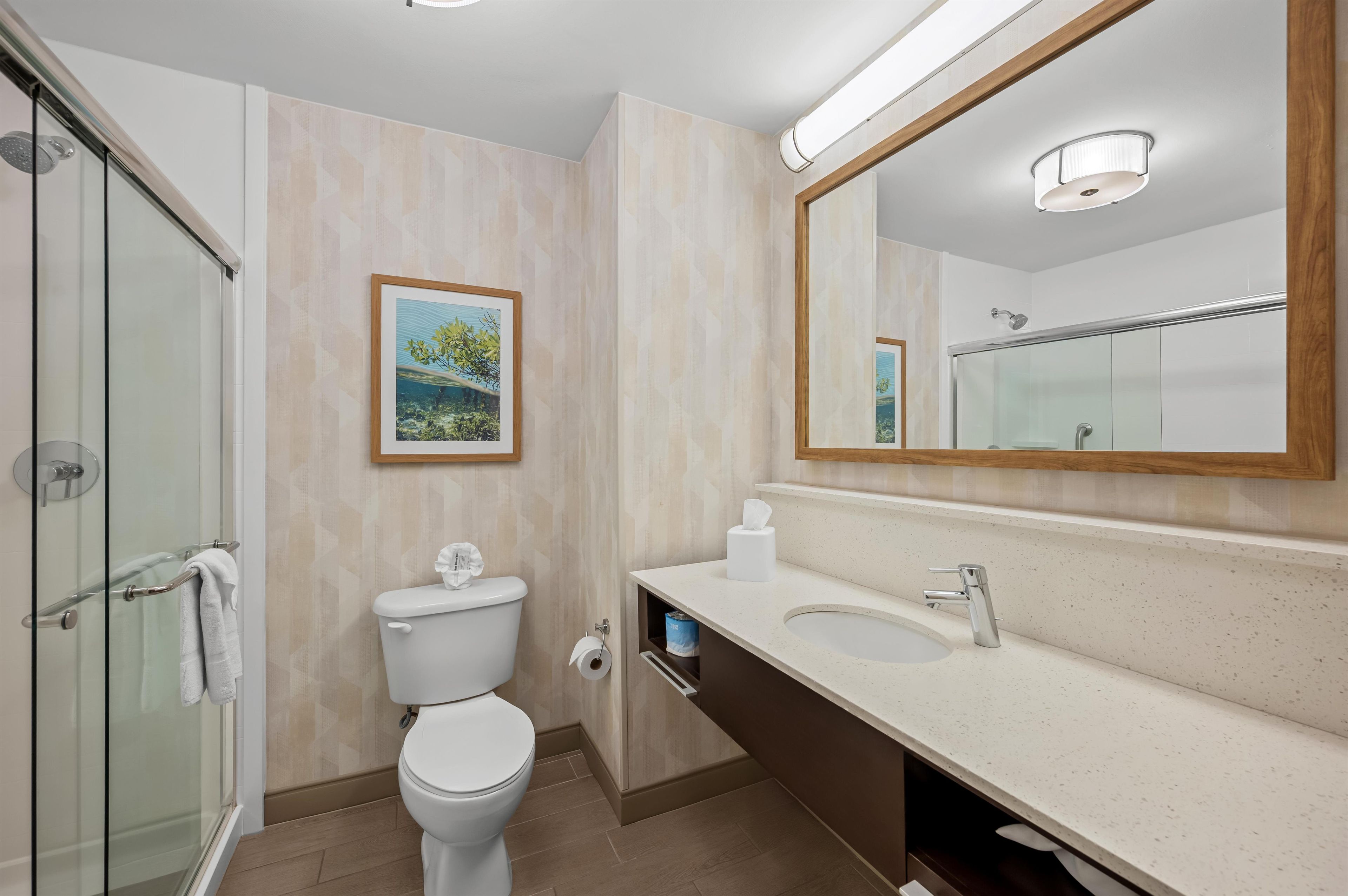 A modern bathroom with a glass shower enclosure, a toilet, a sink, and a large mirror.