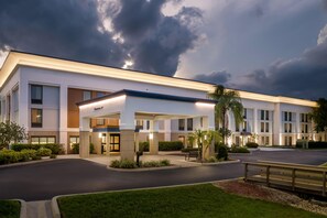 A modern hotel with a covered entrance, a parking lot, and well-maintained landscaping.