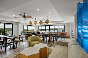 A modern hotel lobby with a dining area, seating, and a view of the outdoors.