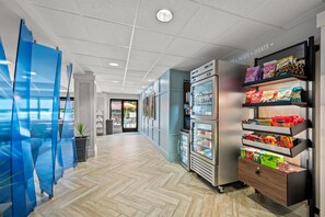 Un pasillo con una máquina expendedora, un refrigerador y una pared con un letrero.