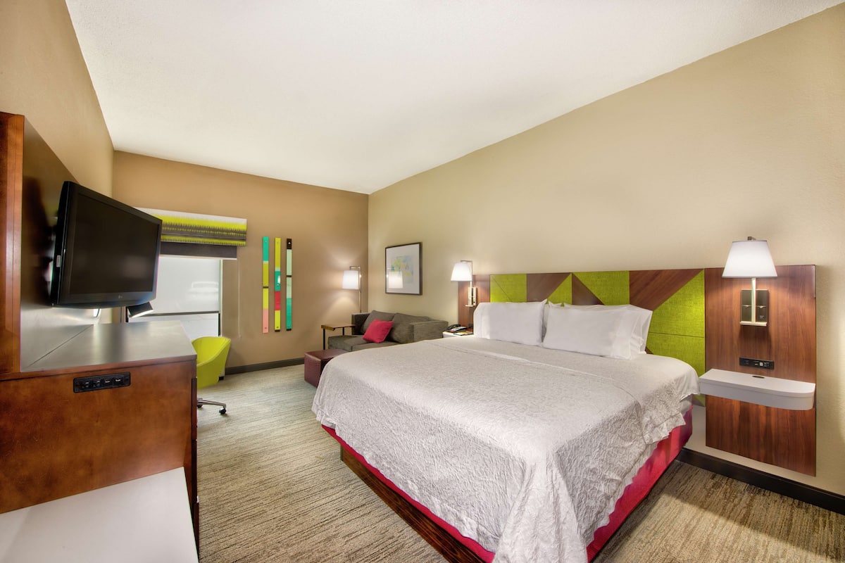 A hotel room with a large bed, a desk with a television, a chair, and a small table.