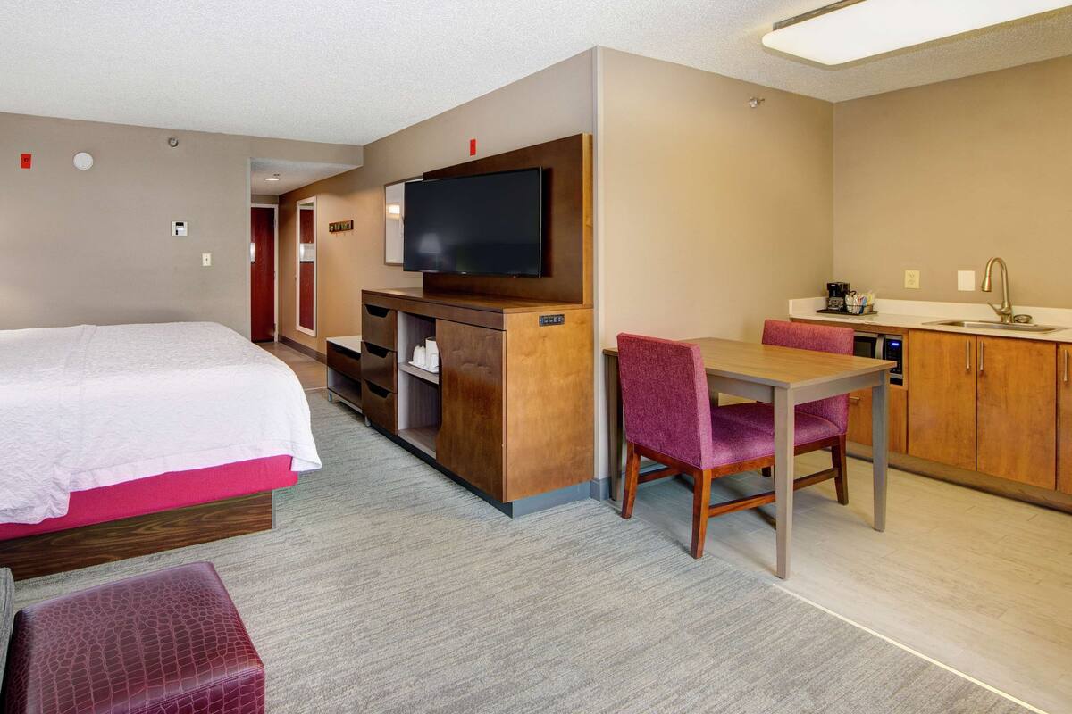 A hotel room with a bed, a desk, a TV, and a kitchenette.