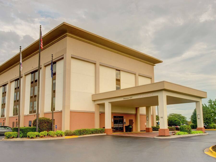 A hotel with a covered entrance, a flagpole with an American flag, and a sign for the Hampton Inn.