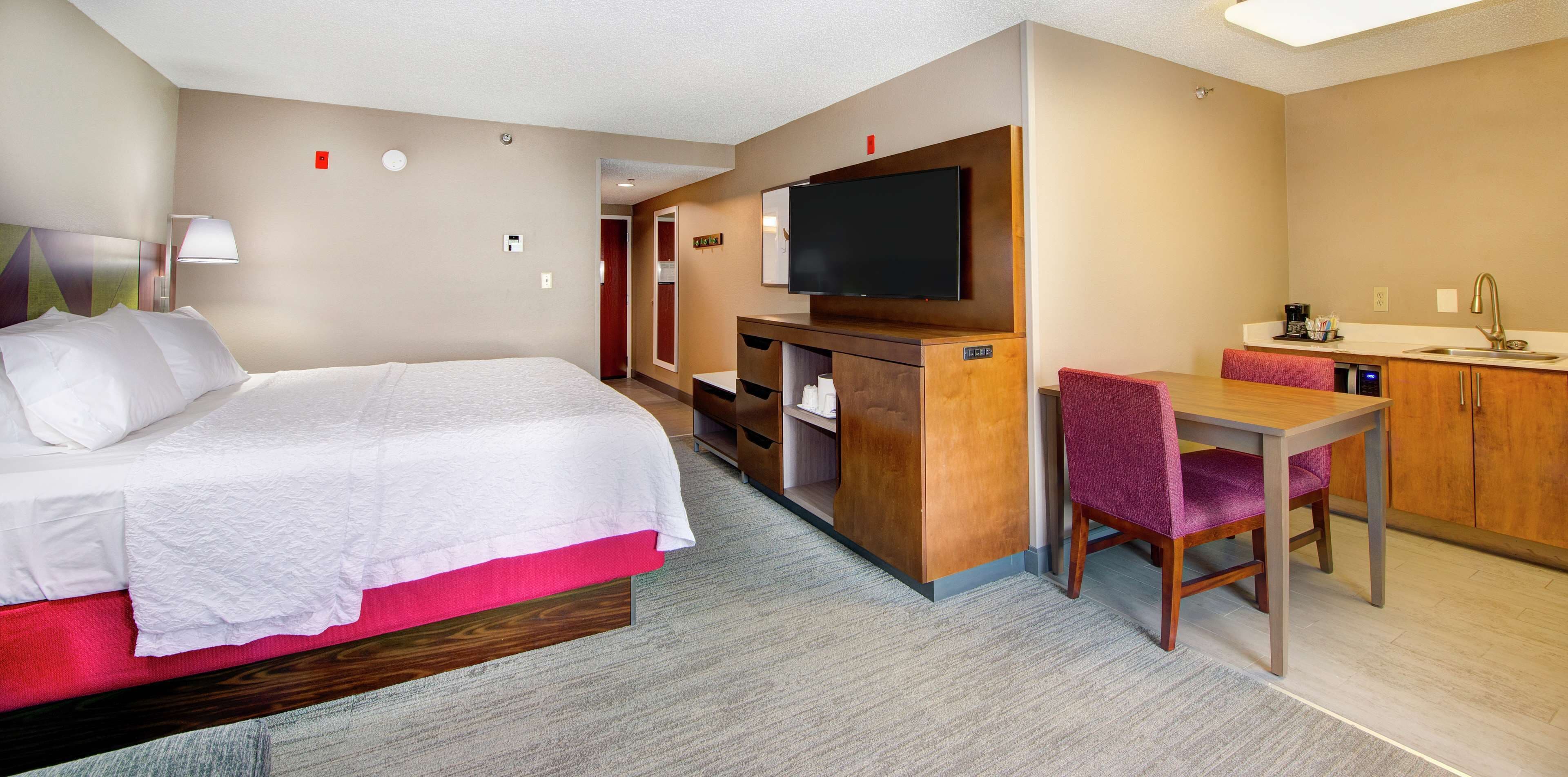Une chambre d’hôtel équipée d’un lit, d’un bureau, d’une télévision, d’un lavabo et d’un miroir.