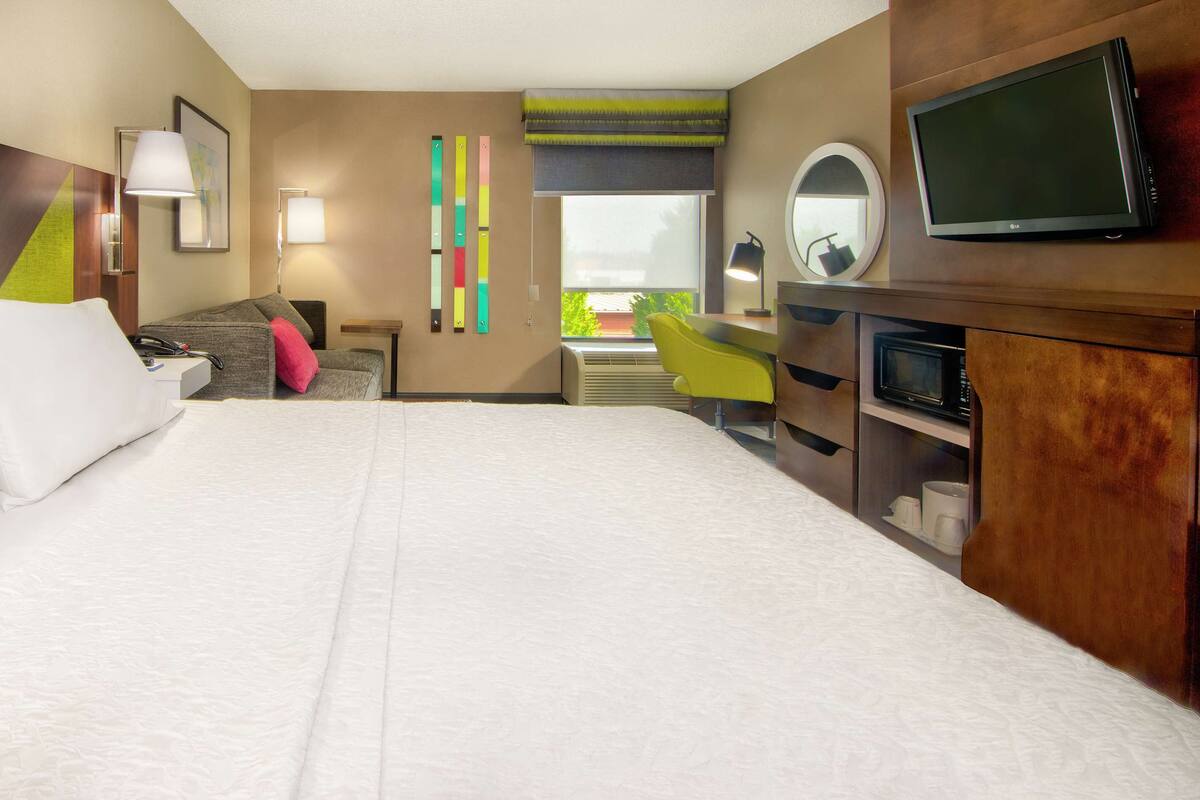 A hotel room with a large bed, a desk with a chair, a television, and a window with a view.