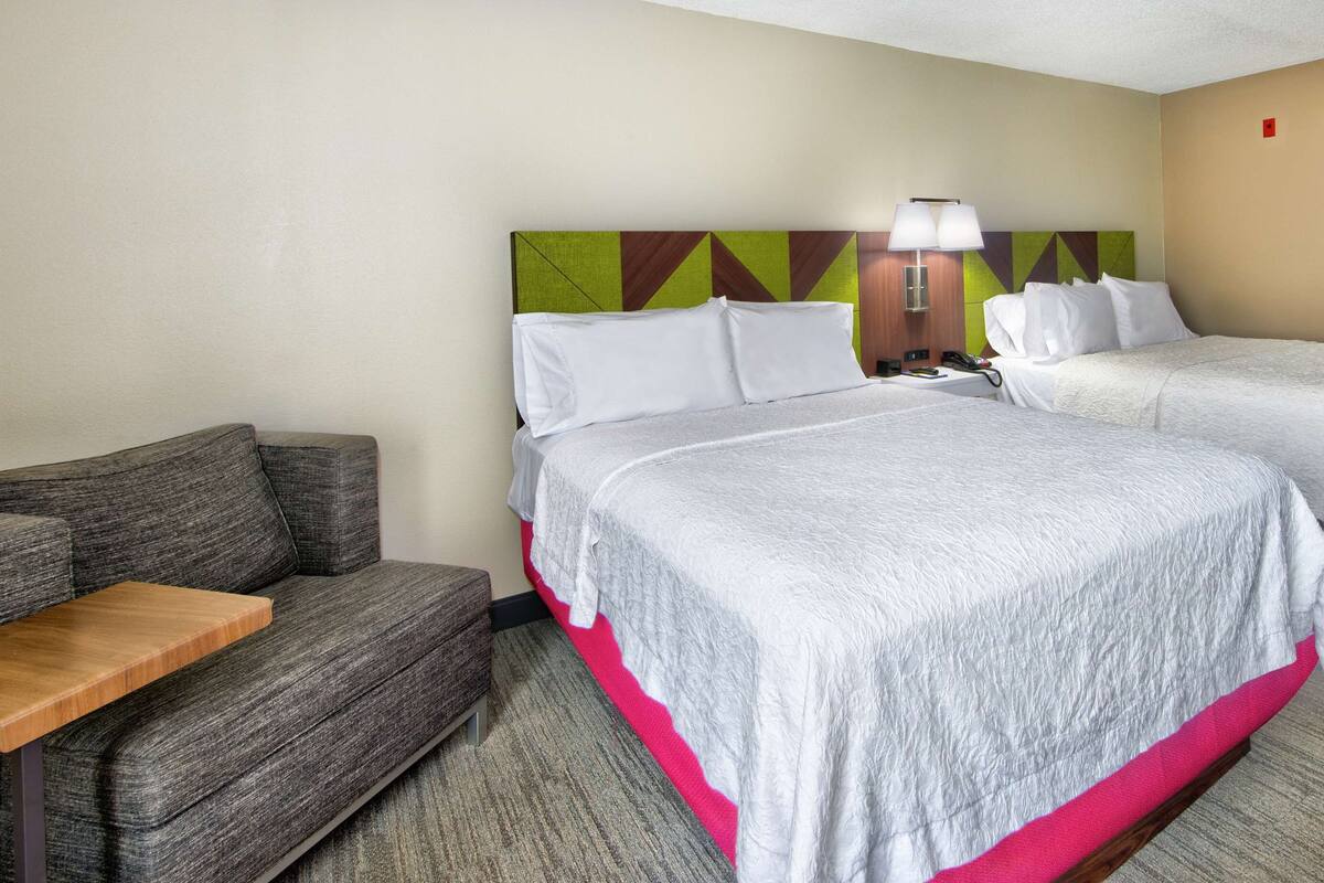 A hotel room with two beds, a sofa, a small table, and a chair.
