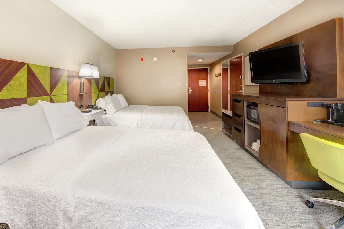 A hotel room with two beds, a TV, a desk with a chair, and a bathroom door.
