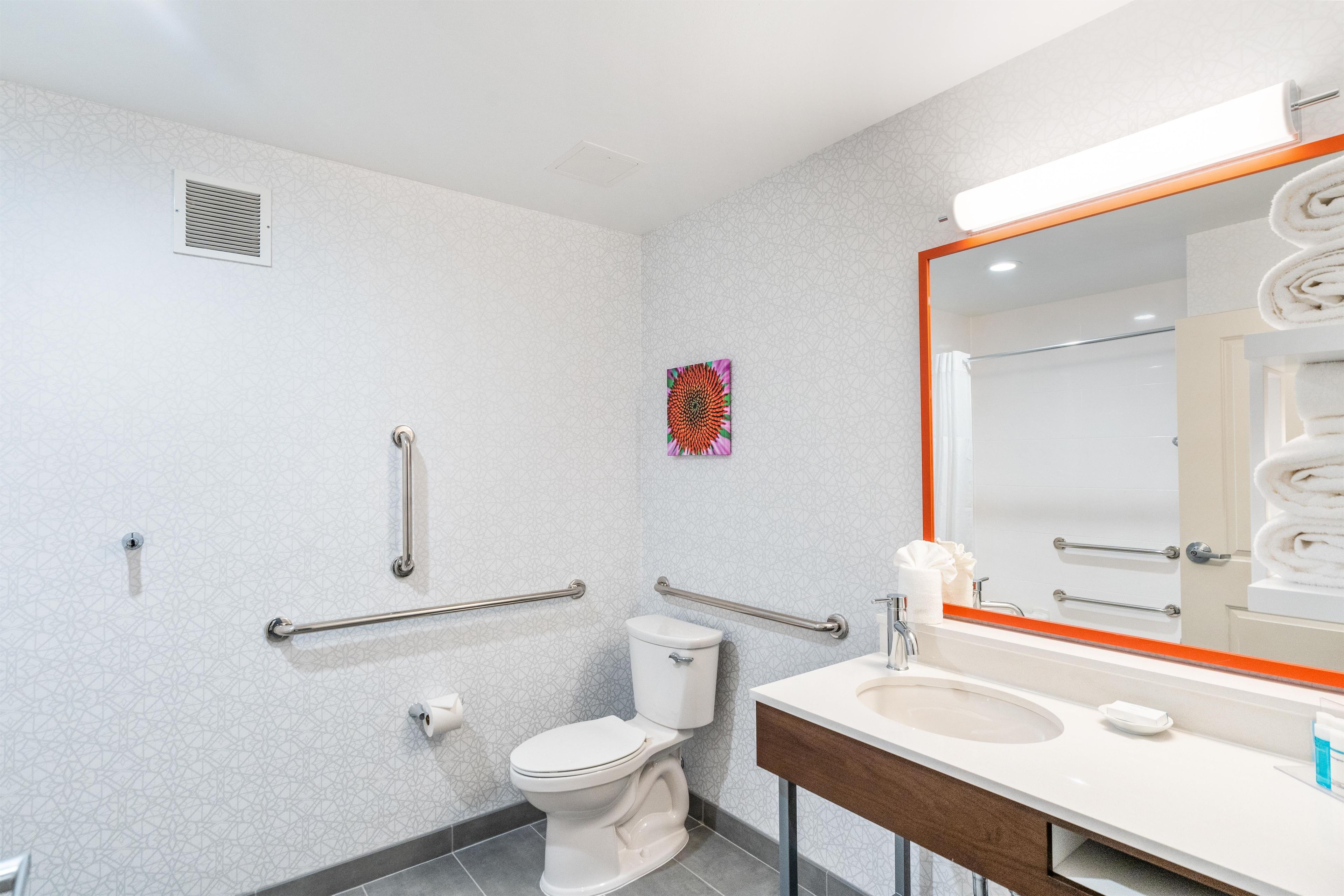 Ein Badezimmer mit Toilette, Waschbecken, Spiegel und Haltegriffen.