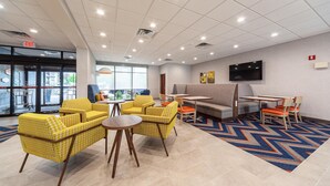 A lobby with yellow patterned chairs, a round table, a TV on the wall, and a patterned rug. - Hampton Inn Winchester N/Conference Center, VA (Winchester)
