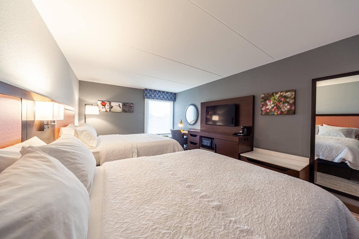 A hotel room with two beds, a TV, a desk, and a large mirror.