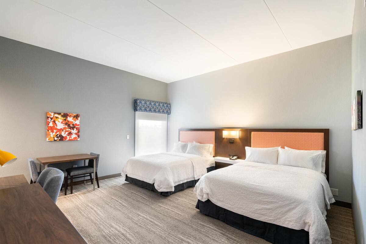 A hotel room with two beds, a desk, and a chair.