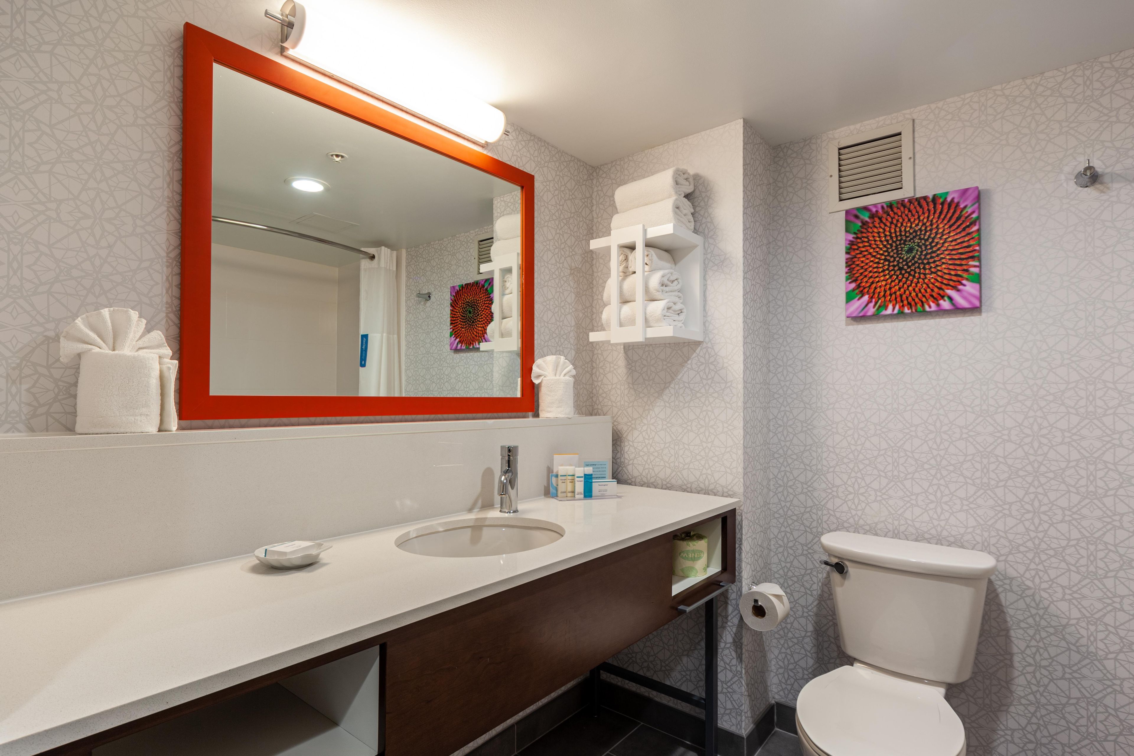 Un baño con un espejo grande, un lavamanos, un inodoro y un perchero para toallas.