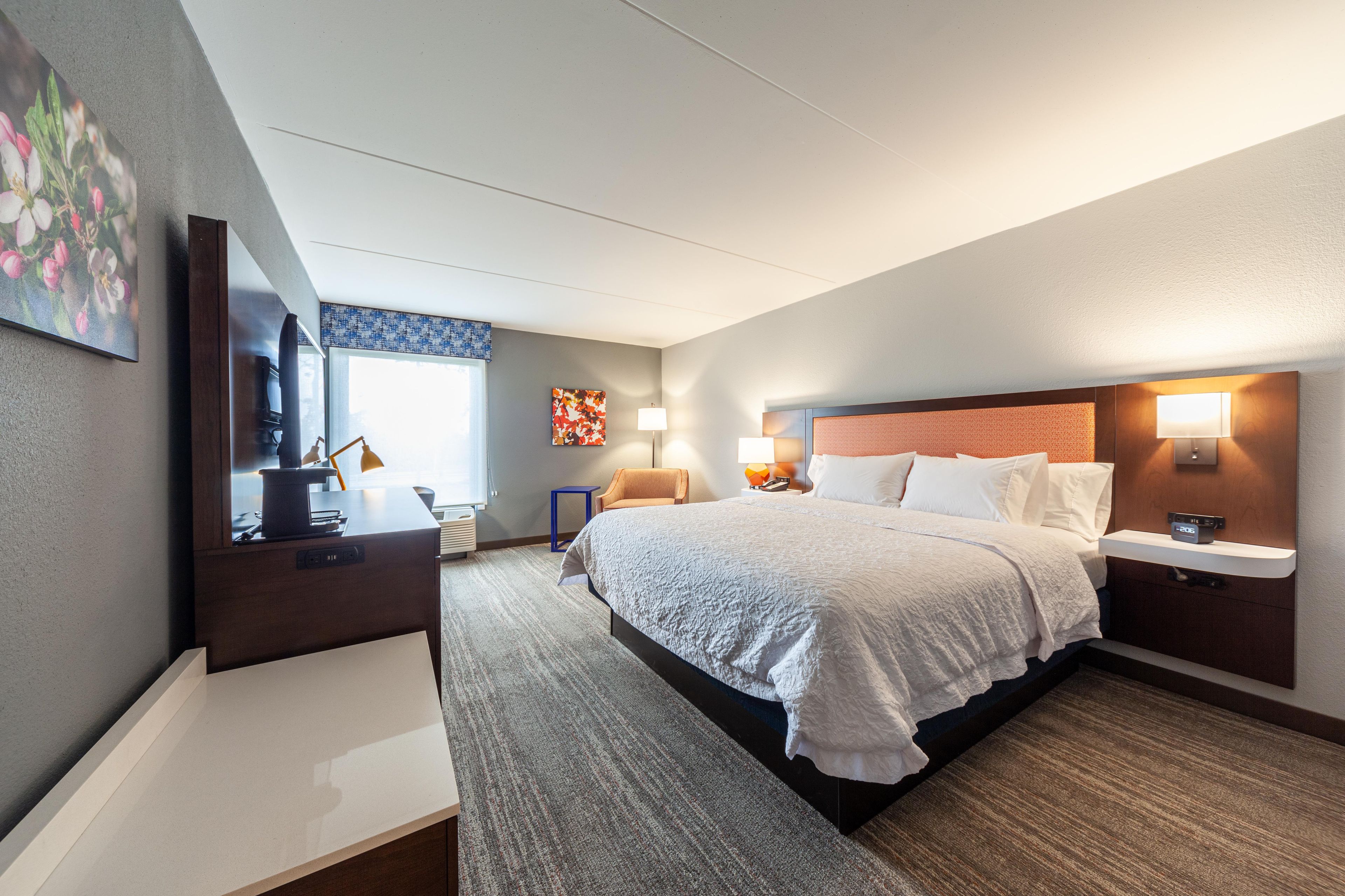 A hotel room with a large bed, bedside tables, a desk, and a mirror.