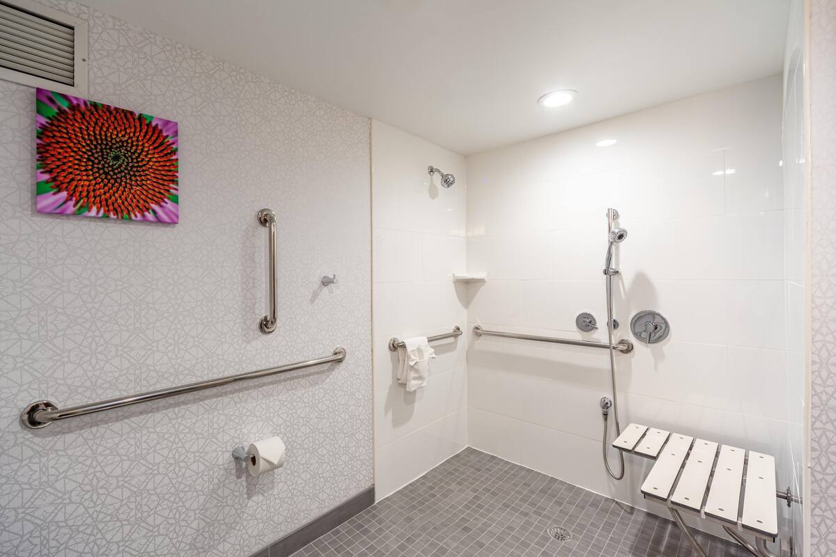 A bathroom with a shower, grab bars, a hand dryer, and a towel rack.