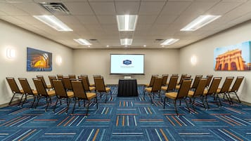 A conference room with a projector screen, arranged chairs, and a carpeted floor.