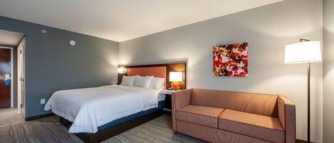 A hotel room with a bed, a sofa, a lamp, and a wall art piece.