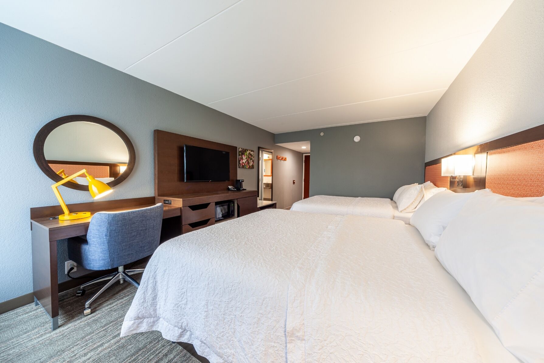 Een hotelkamer met twee bedden, een bureau met stoel, een televisie en een spiegel.