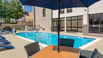 A swimming pool with lounge chairs and a table, surrounded by a fence and a building with large windows.
