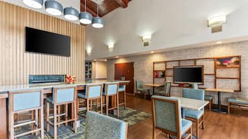 A modern bar area with a flat-screen TV, wooden panel walls, and blue upholstered chairs.
