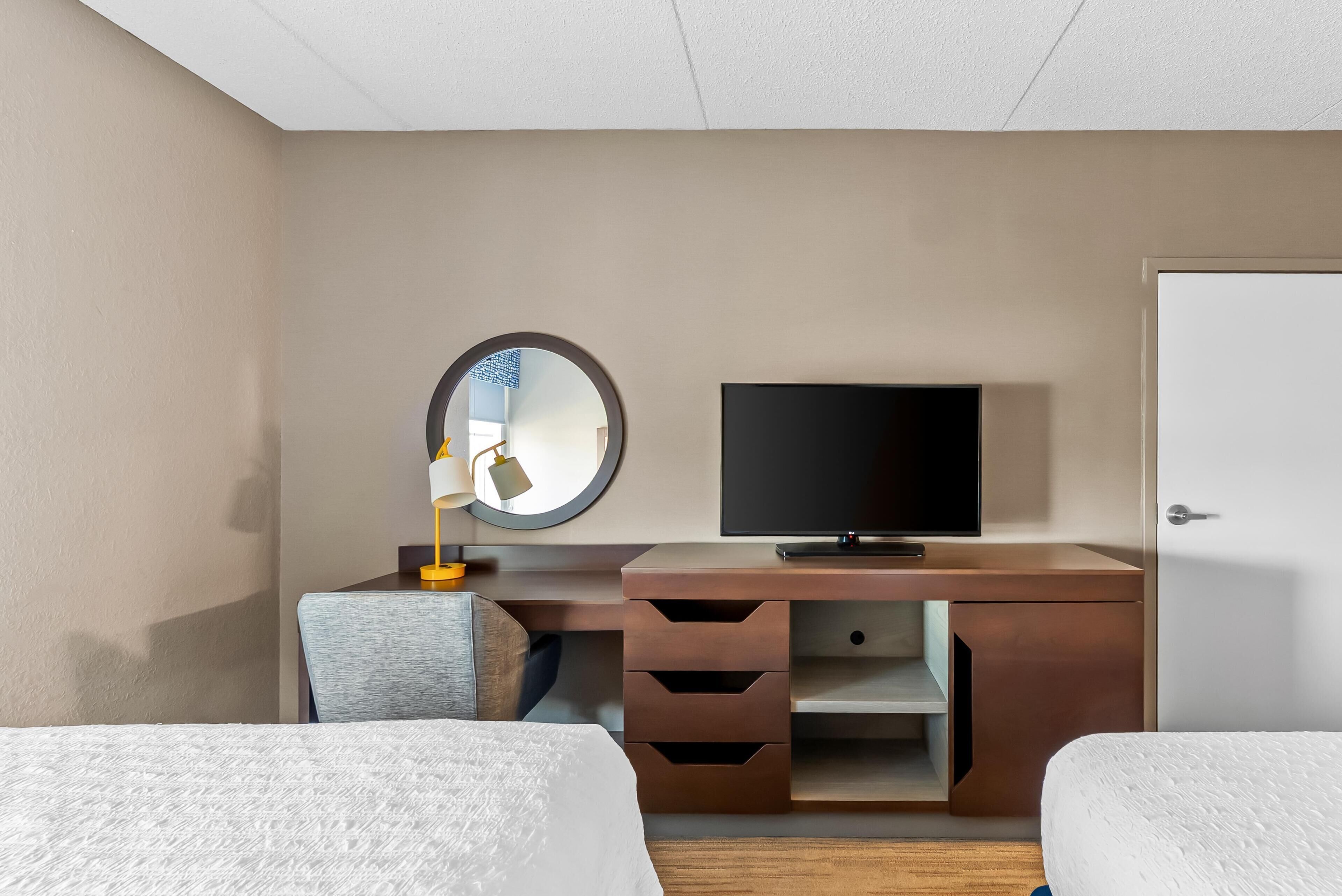 Una habitación de hotel con una cama, un escritorio con televisor, un espejo y una puerta.