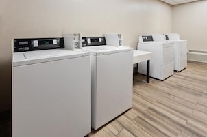 A laundry room with three white front-loading washers and dryers, a control panel, and a wooden floor.