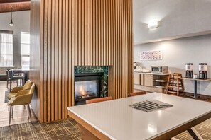 A modern interior with a fireplace, wooden panel wall, bar area, and kitchen with coffee machines.