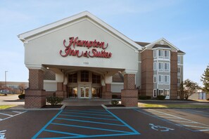Un hôtel Hampton Inn & Suites avec une façade en briques, de grandes portes d’entrée et un parking aménagé pour les personnes à mobilité réduite.
