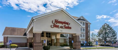 A Hampton Inn & Suites building with a brick facade, large windows, and a parking lot with handicapped-accessible spaces.
