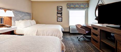 A hotel room with two beds, a desk with a computer, a TV, and a chair.