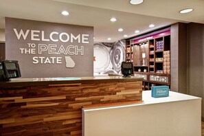 A reception desk with a 'Welcome to the Peach State' sign, a wooden reception area, and a display of local products. - Hampton Inn Atlanta-Mall Of Georgia (Buford)
