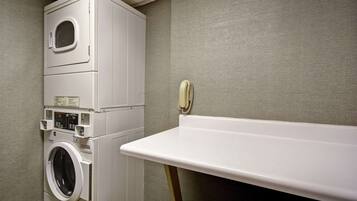 A compact laundry area with a stacked washer and dryer, a small ironing board, and a wall-mounted telephone.