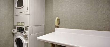 A compact laundry area with a stacked washer and dryer, a small ironing board, and a wall-mounted telephone.