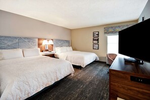 A hotel room with two beds, a TV, a desk, a lamp, and artwork on the wall.