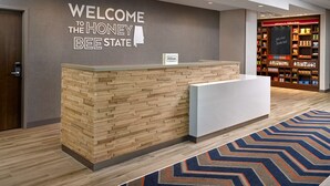 Uma receção com design de painel de madeira, um letreiro que diz "WELCOME TO THE HONEY BEE STATE" e uma exposição de produtos locais ao fundo.