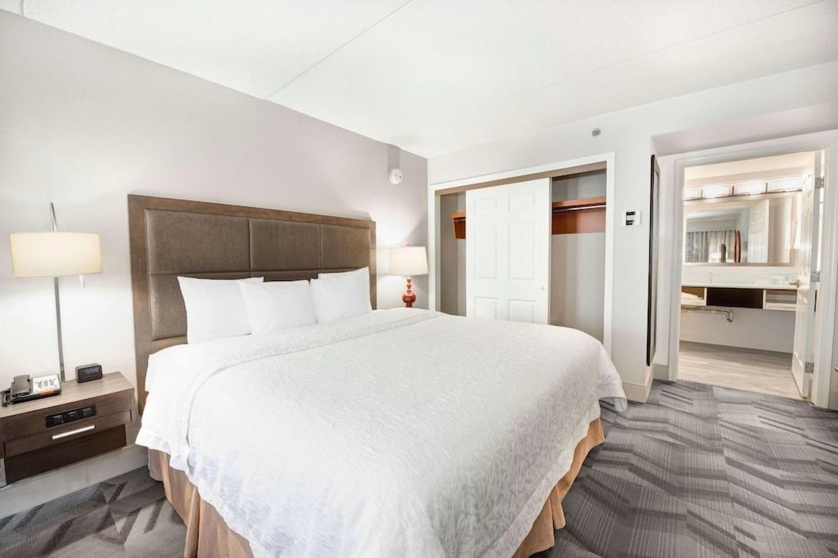 A hotel room with a large bed, bedside tables, a nightstand, a lamp, and a wardrobe.