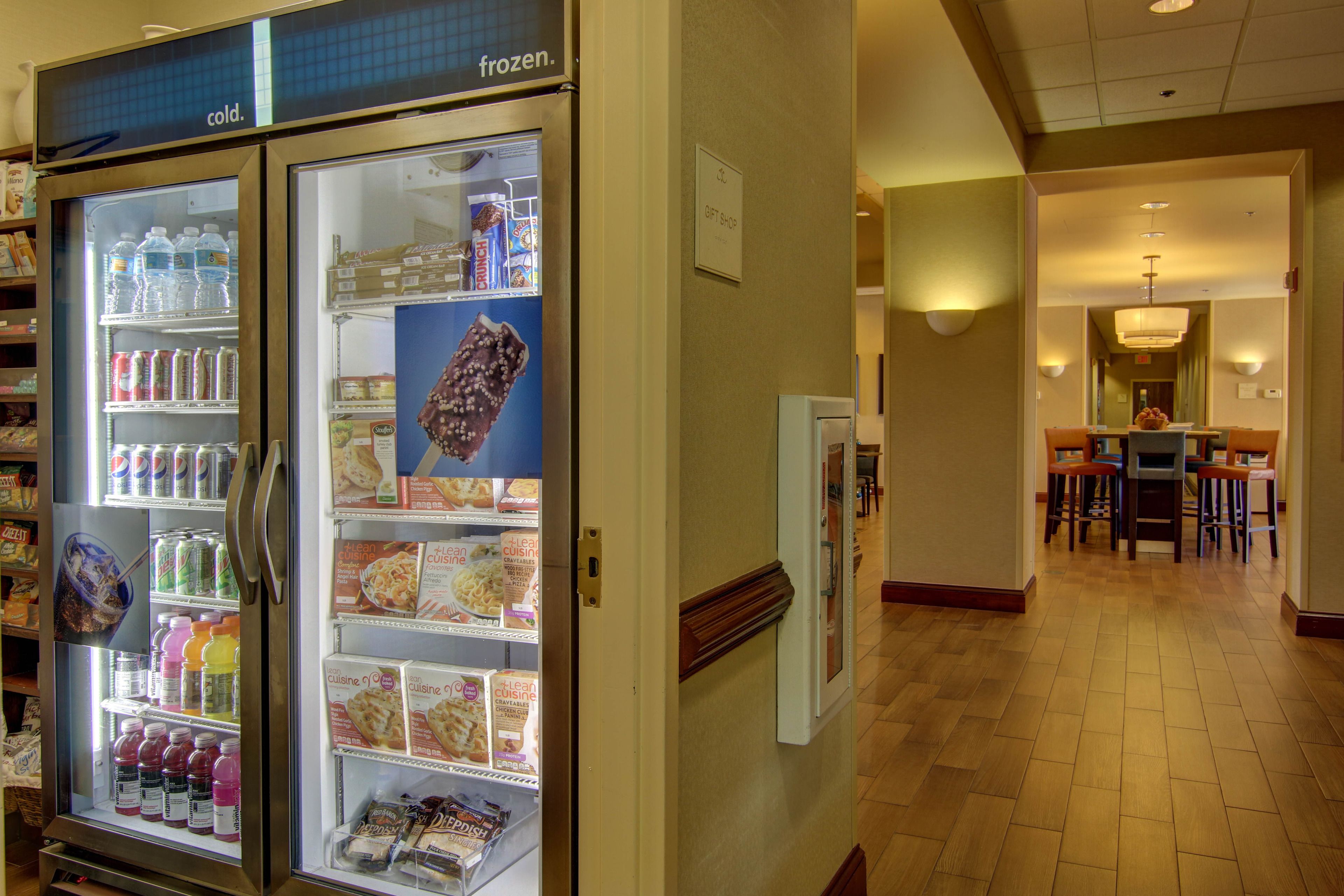 A hotel corridor with a refrigerated display case stocked with beverages and food items.