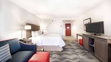 A hotel room with a bed, a TV, a desk, a lamp, and a sofa.