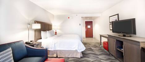 A hotel room with a bed, a TV, a desk, a lamp, and a sofa.