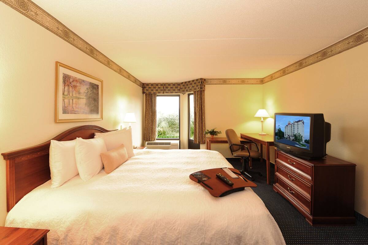 A hotel room with a large bed, a desk with a chair, a television, and a window with curtains.