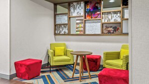 Una habitación con dos sillones verdes estampados, una mesita redonda pequeña y un pouf rojo.